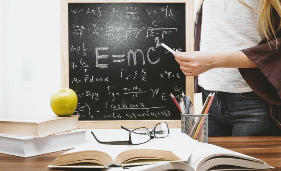 učitelka před tabulí s napsanými vzorci před stolem s knihami