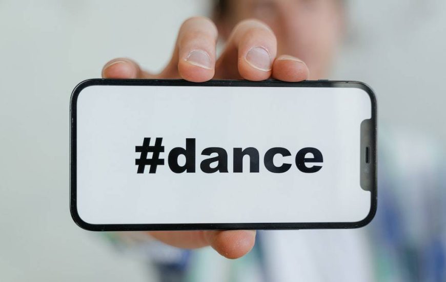 muž drží telefon na němž je nápis #dance